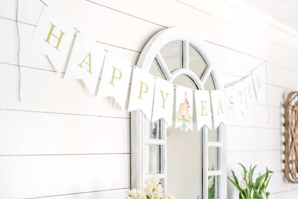 Happy Easter free printable banner in a dining room over a wood buffet