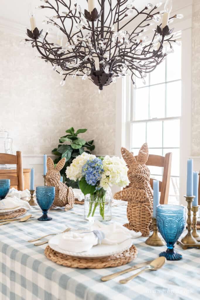 Coastal blue and white Easter table setting with wicker bunnies, hydrangeas, and cobalt goblets.