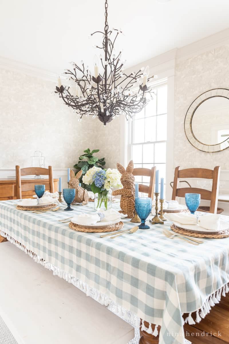 Blue and white Easter tablescape with gingham tablecloth and wicker bunnies. 