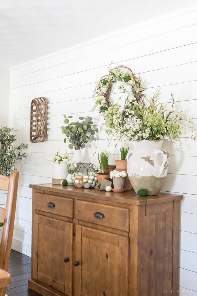 Sideboard buffet with flowerpots, spring flowers, and eggs.