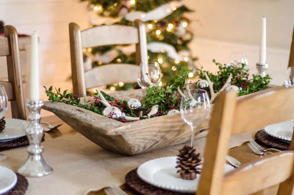 Wooden bowl filled with greenery, red berries, and ornaments for an easy Christmas decorating idea in the dining room
