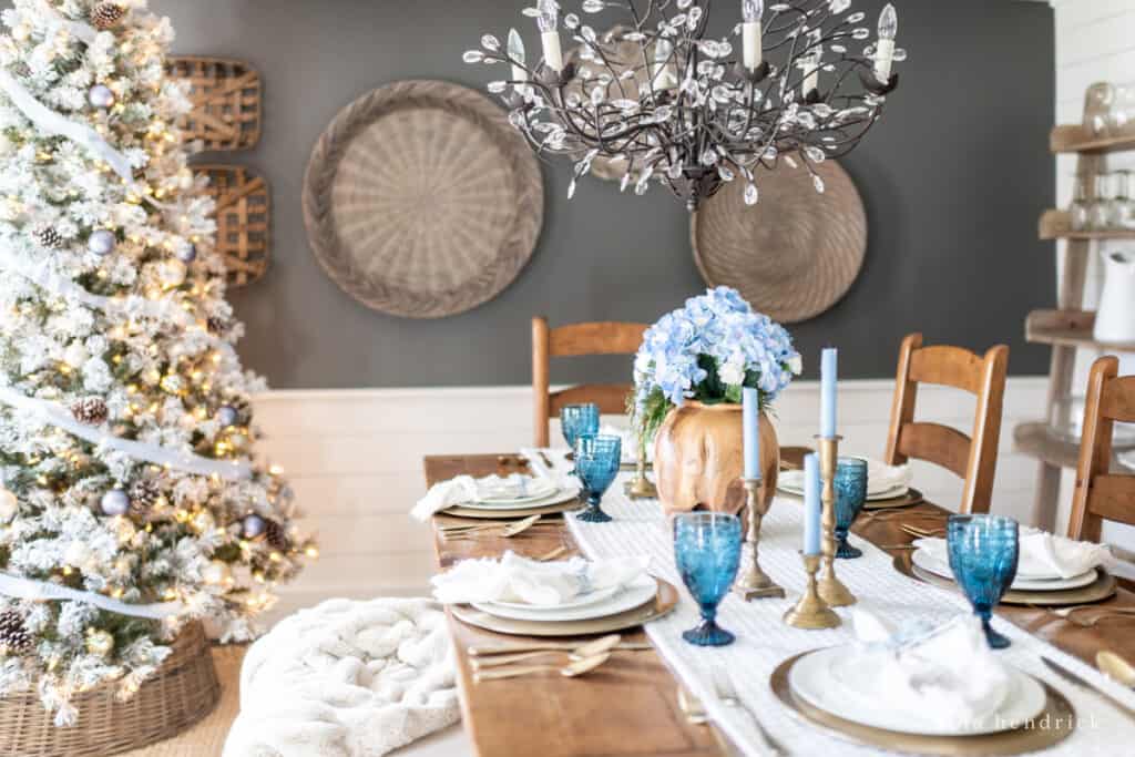 Dining room with blue glasses, flowers, and a white snowy Christmas tree