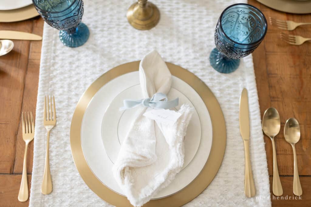 Entertaining essentials for a table setting — white plates, brass charger, white napkin, and flatware