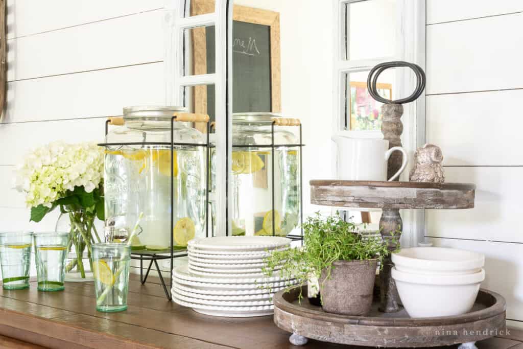 Wood console table covered with entertaining essentials like a drink dispenser and white beaded plates