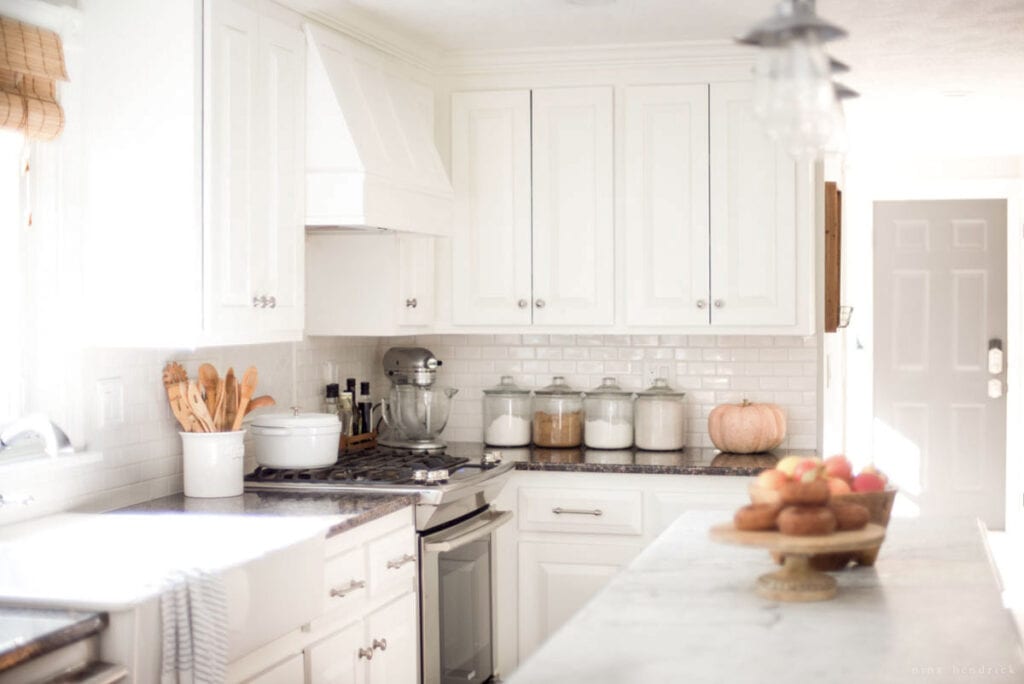 A kitchen with white cabinets and marble counter tops.