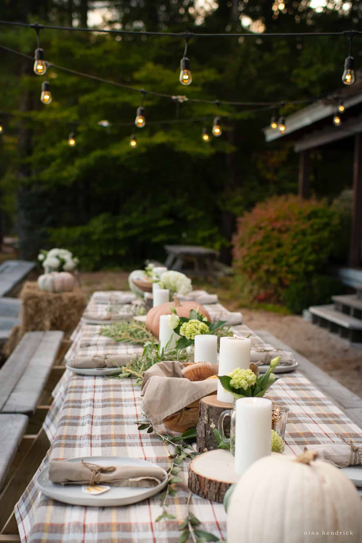 An outdoor table set with pumpkins and a plaid tablecloth.