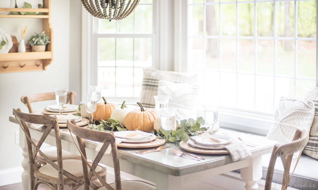 A fall dining room table set with pumpkins and flowers.