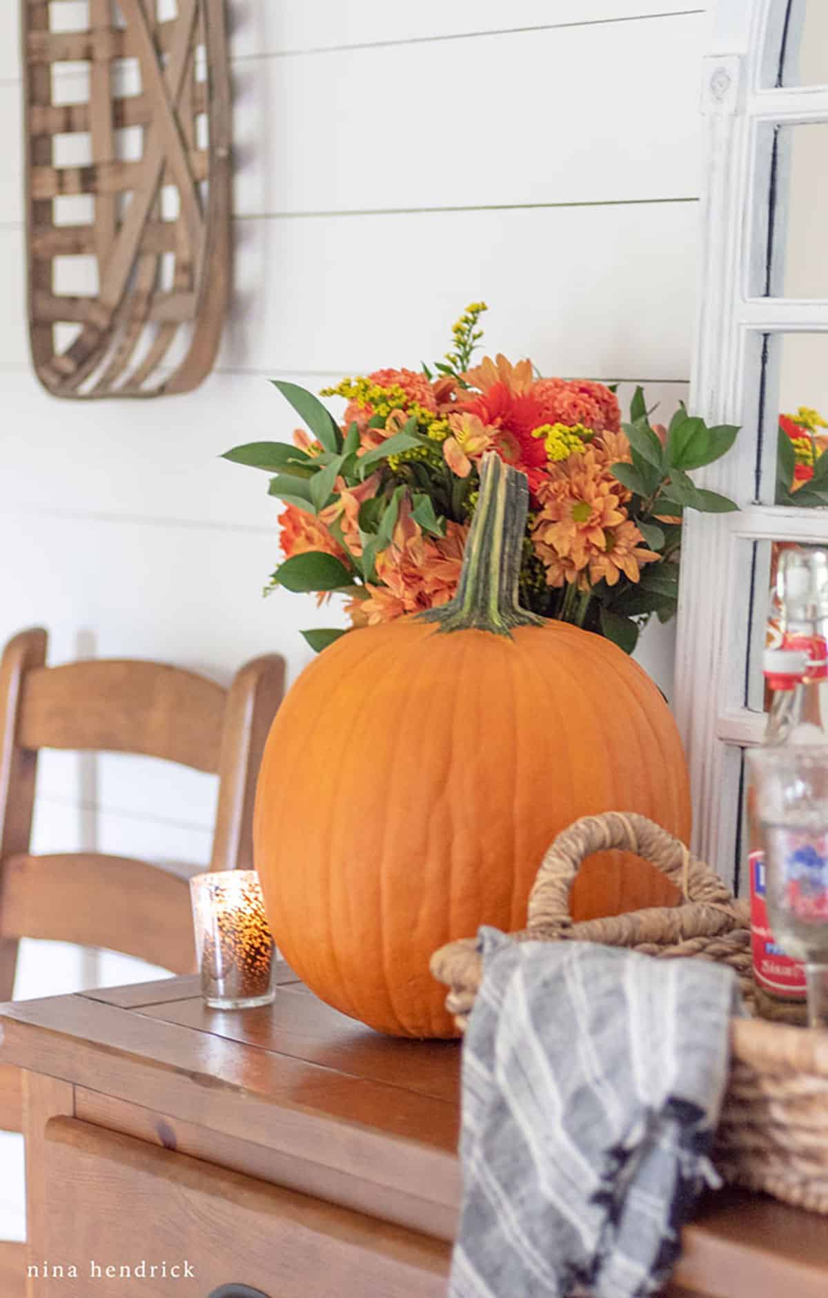 Fall decor ideas featuring a wooden dining room sideboard adorned with an orange pumpkin and flowers