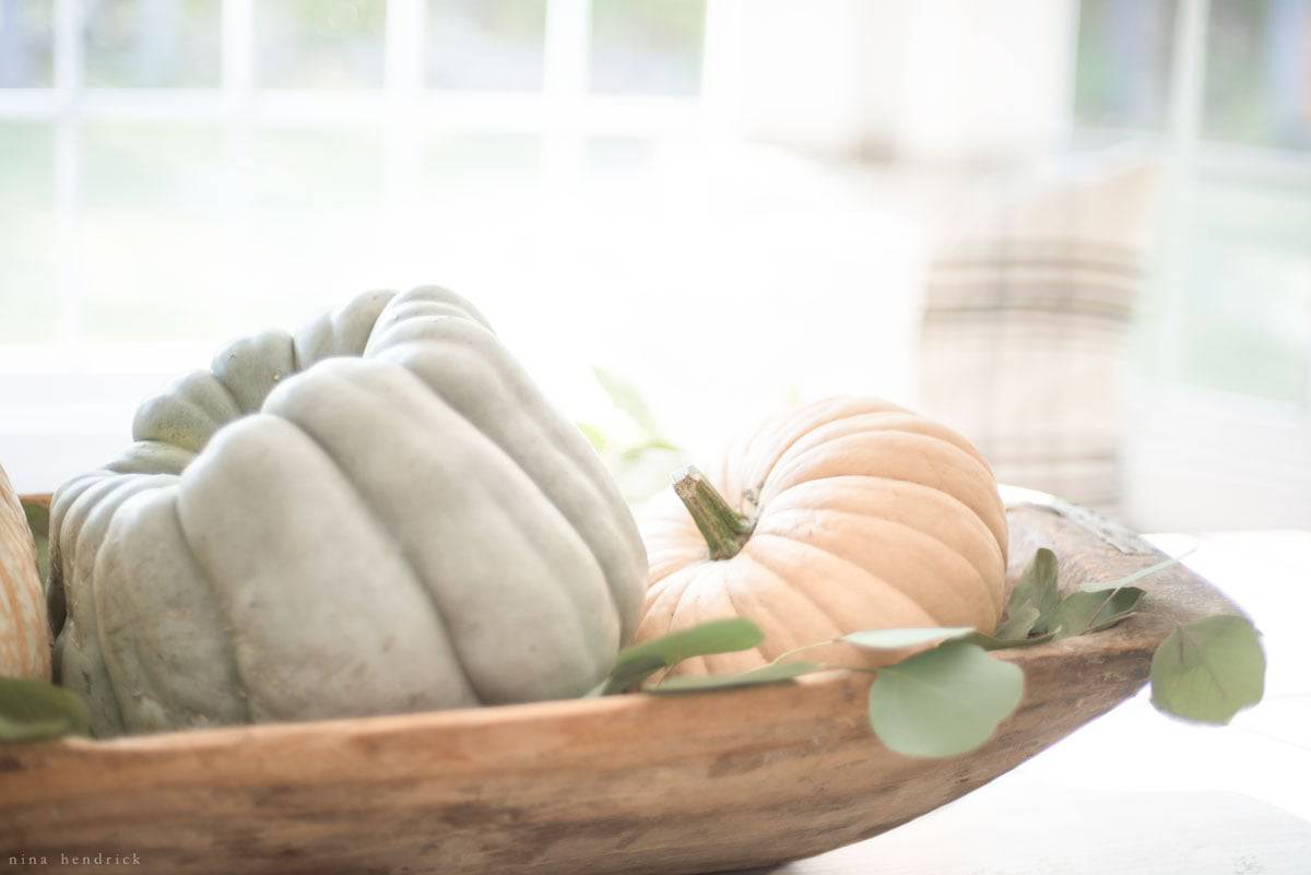 A fall home tour featuring a wooden bowl filled with pumpkins and eucalyptus.