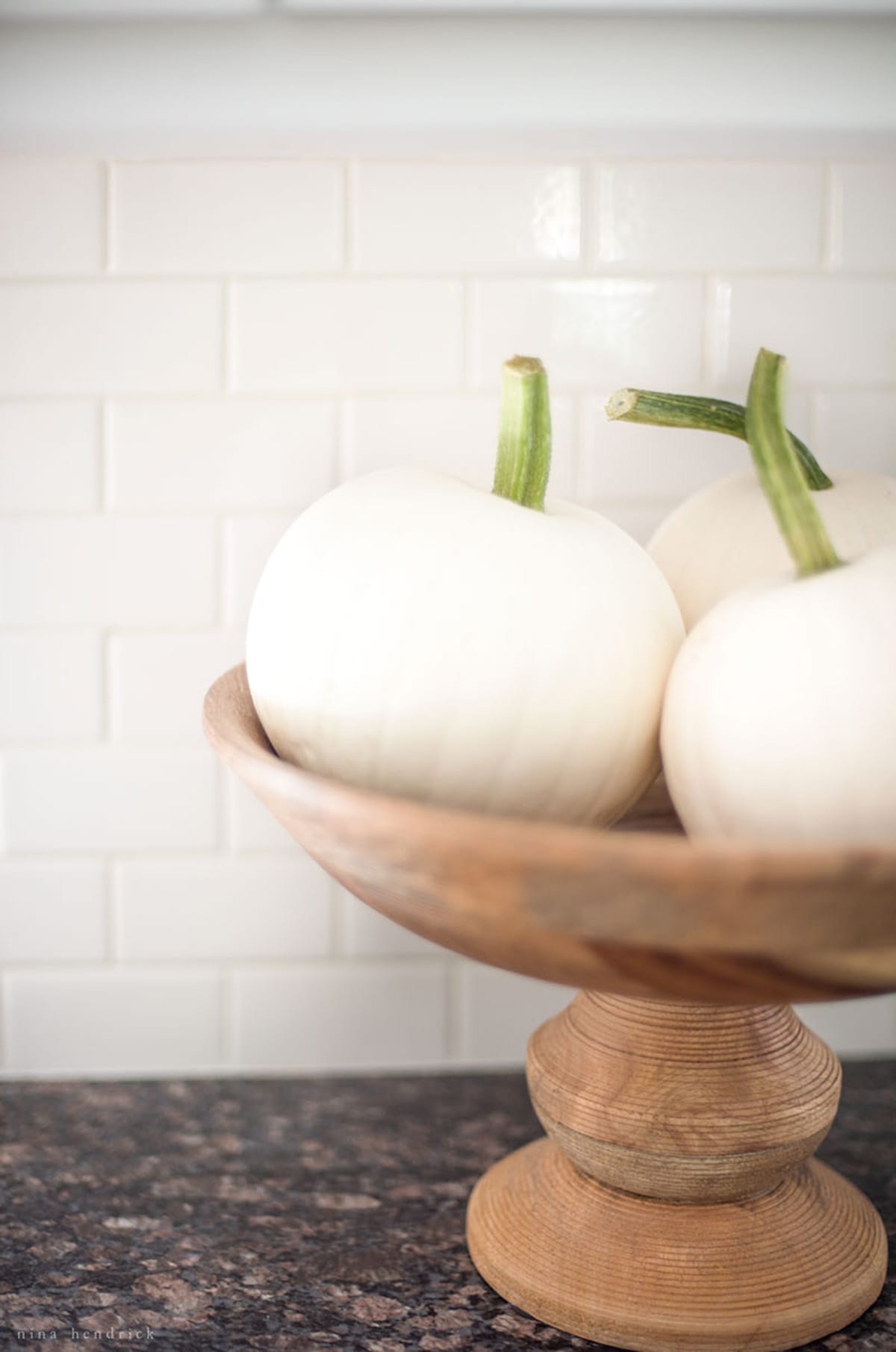 Three white pumpkins in a wooden pedestal bowl.