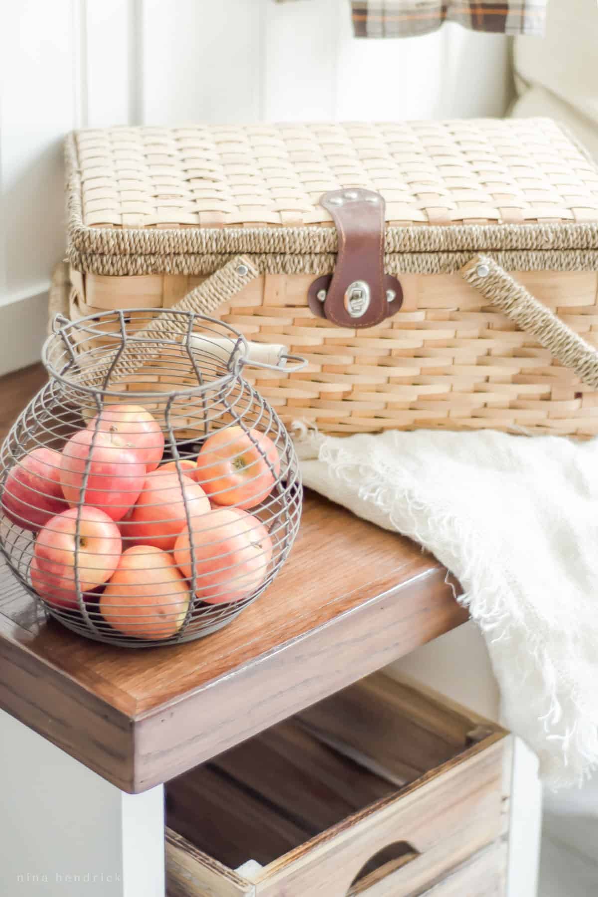 A wicker basket sits on a bench next to apples, adding a cozy touch to the fall home tour.