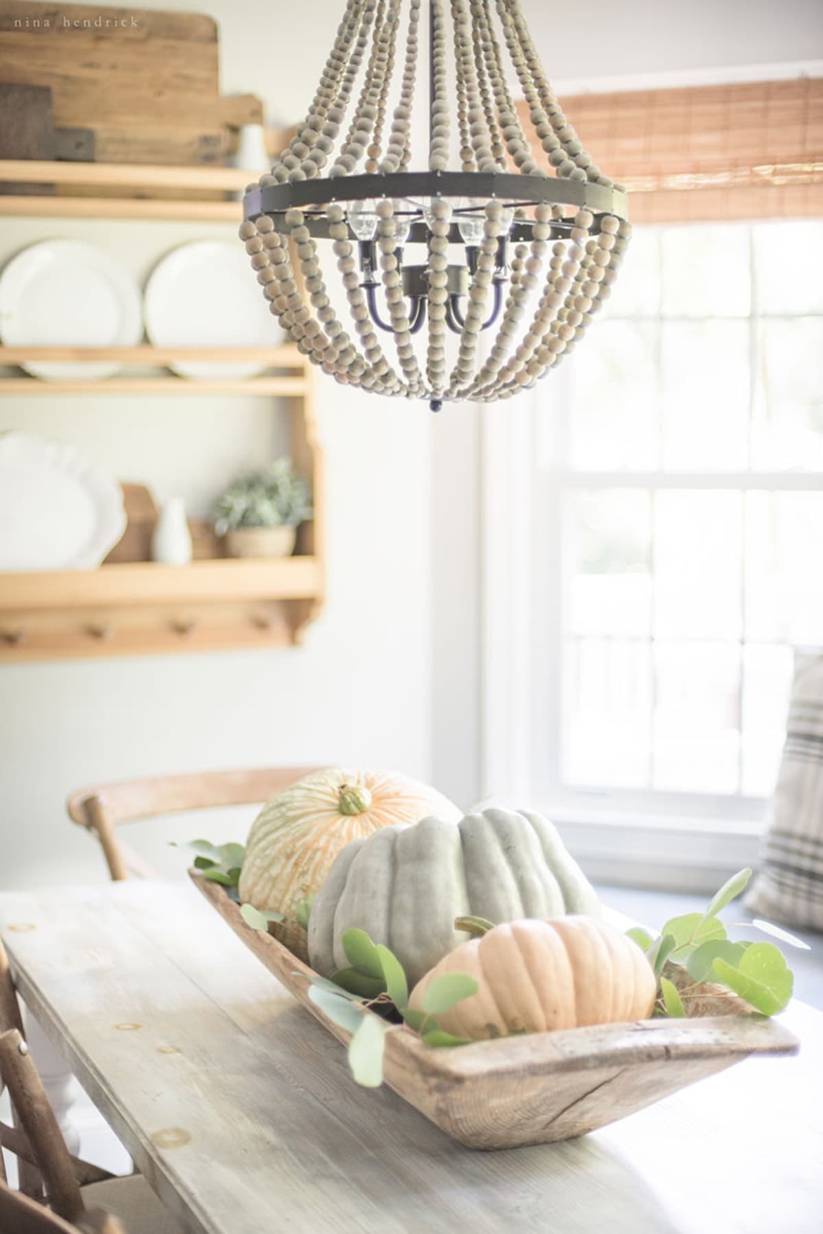 A fall home tour featuring a wooden table adorned with pumpkins and a chandelier.