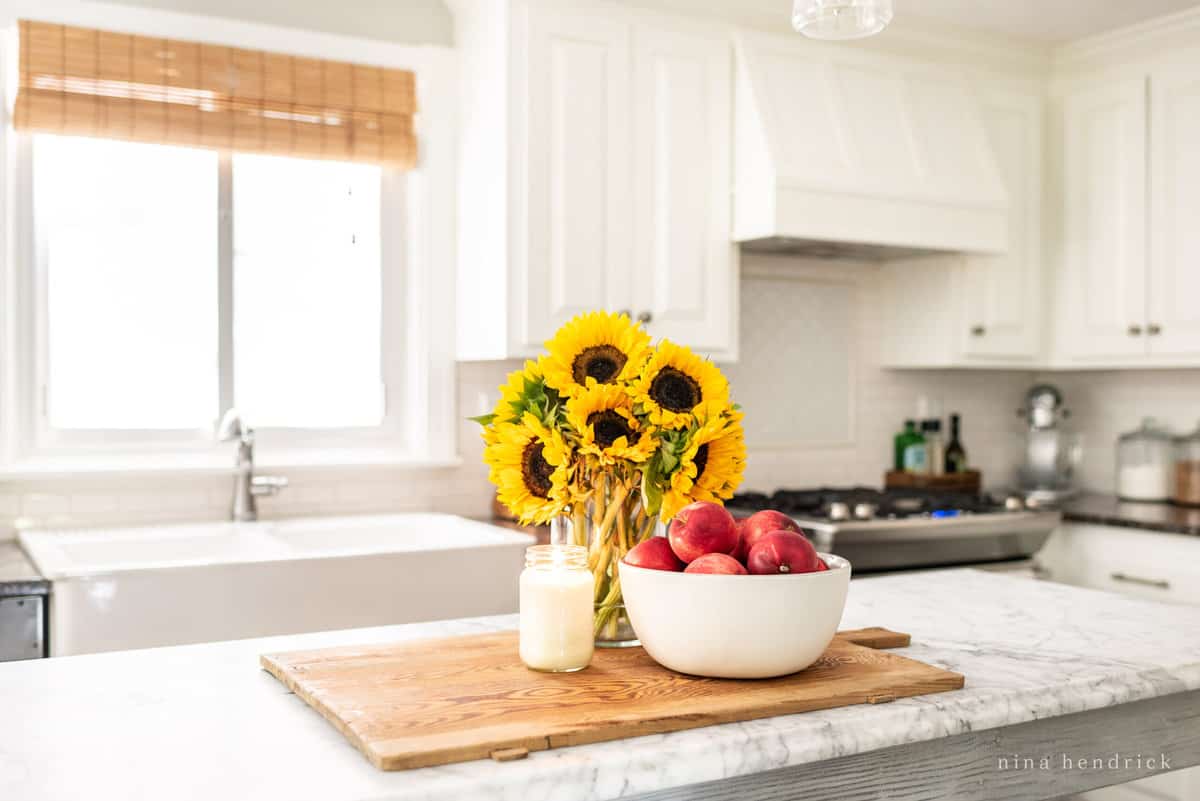 A bowl of apples and sunflowers on a cutting board in a kitchen.