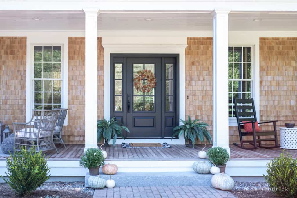 A fall front porch with a black door and pumpkins.