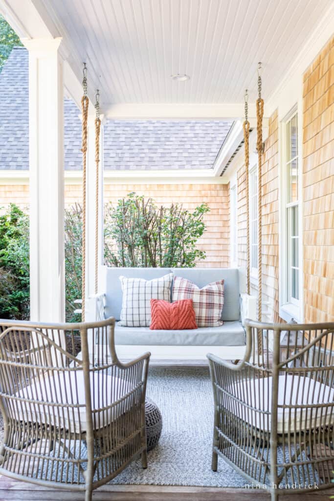 A porch swing with chairs and a fall pillow.