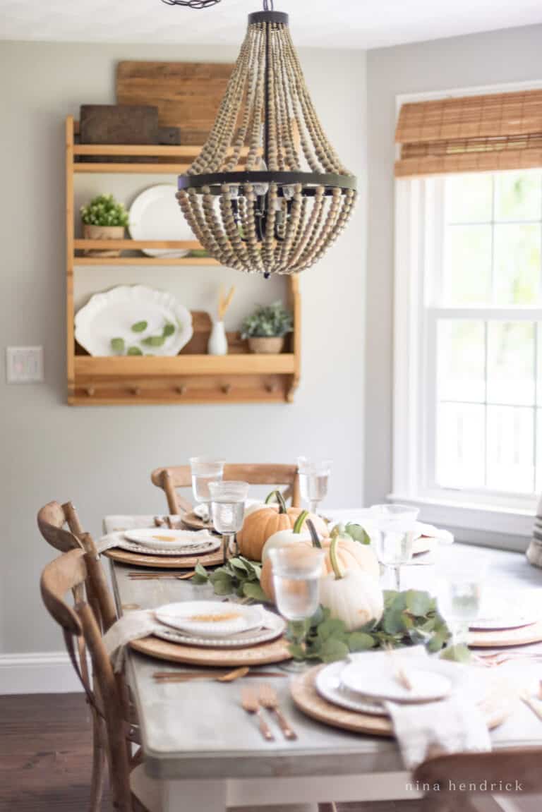 A dining room with a fall tablescape featuring a table, chairs, and a chandelier.