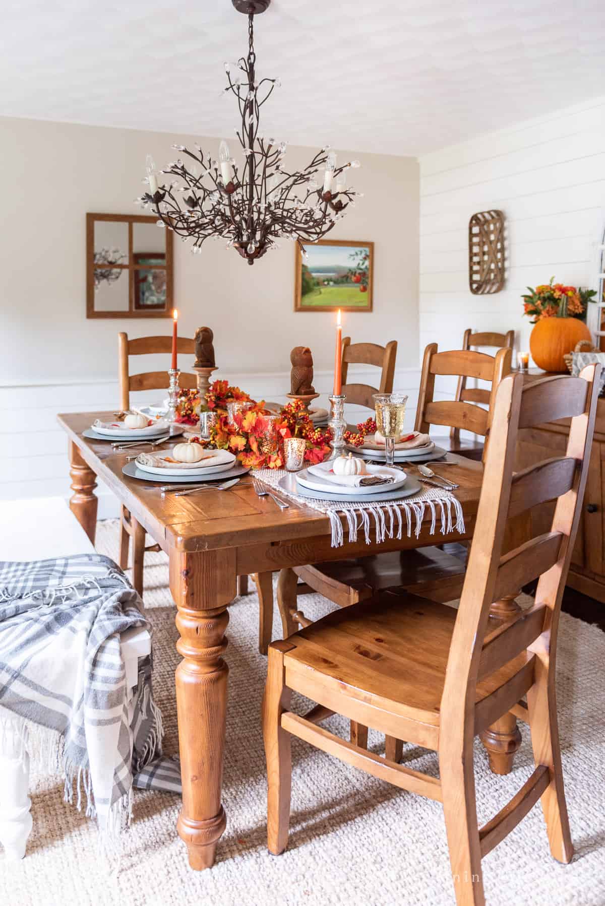 A dining room with a wooden table and chairs decorated with fall table decor.