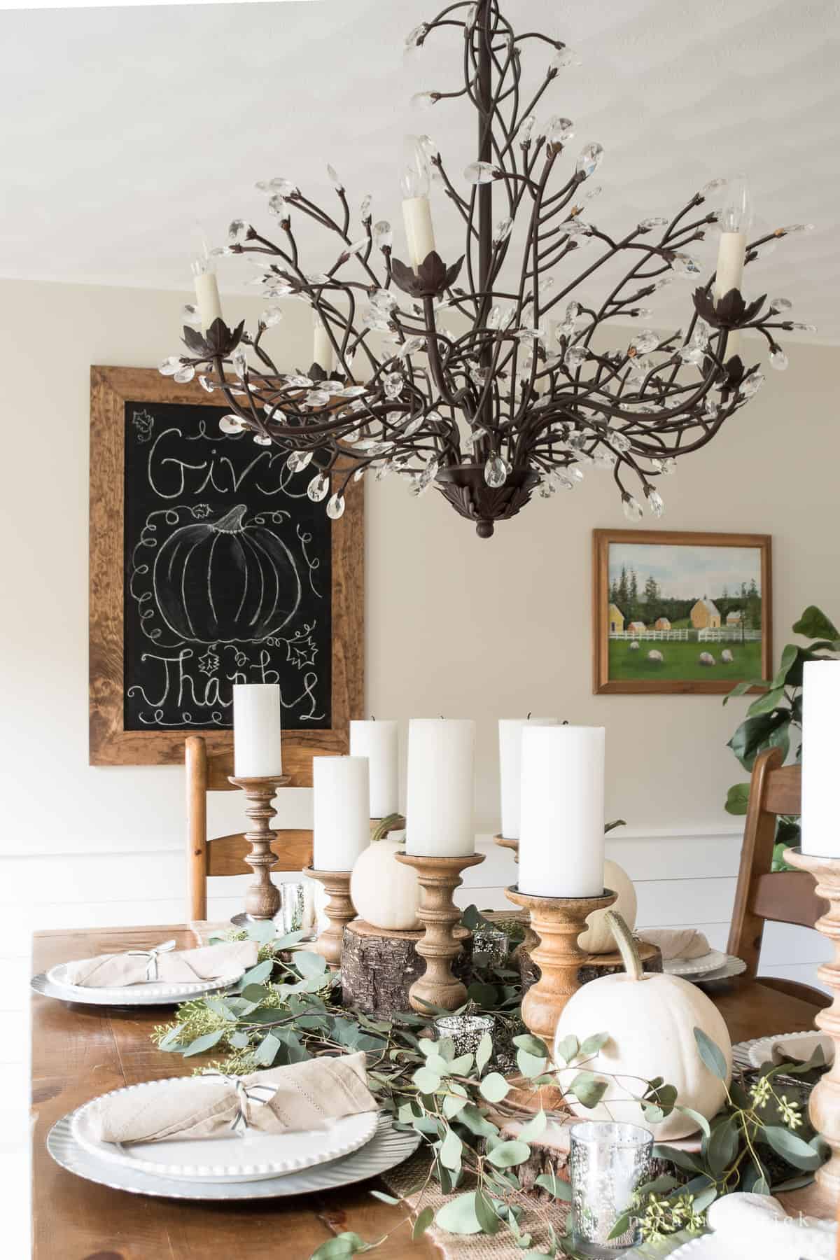 A fall-themed dining room table with a chandelier and pumpkins.