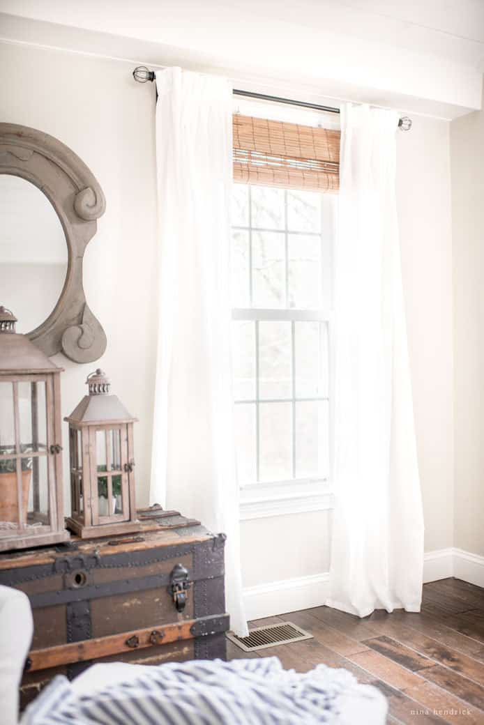 White inexpensive window treatments hanging in white room with light brown roman shades