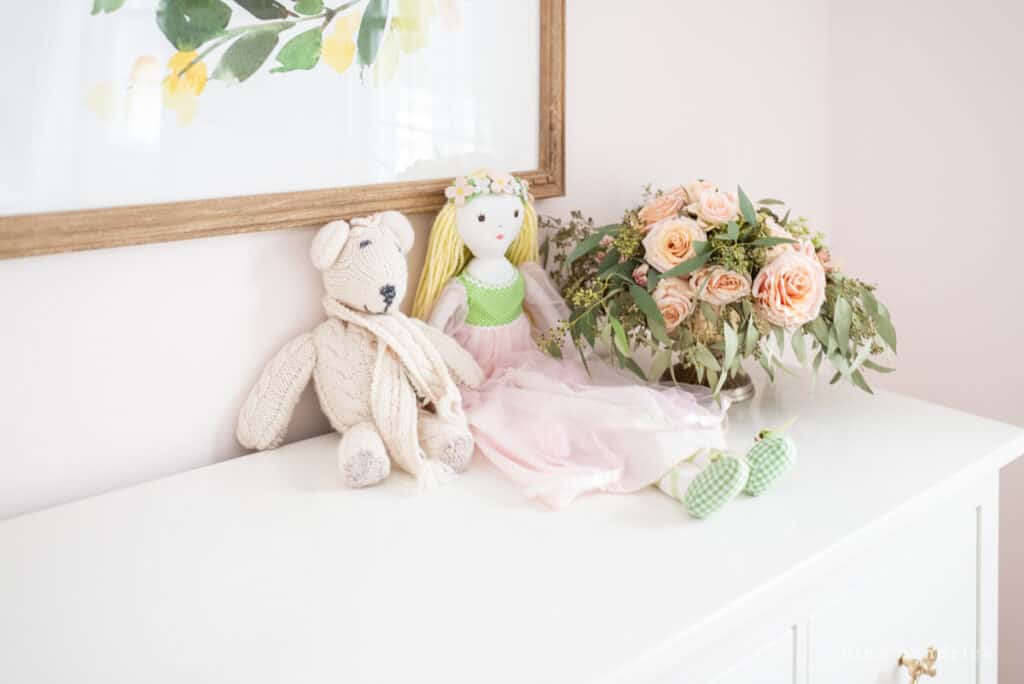 Doll and teddy bear with flowers on a dresser.