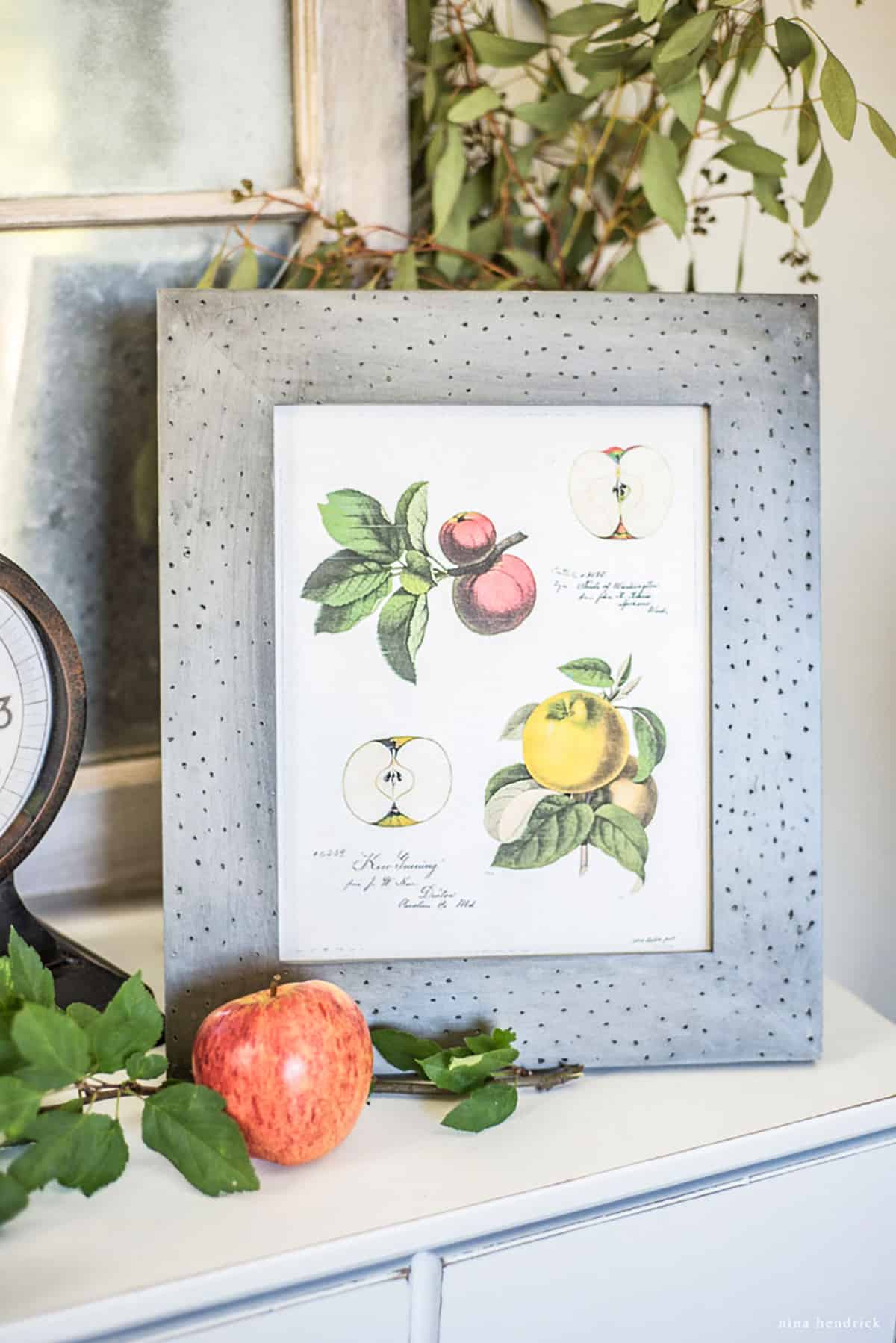 A framed free fall printable of apples and a clock on top of a dresser.