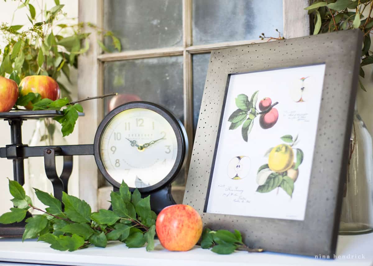 A vignette with apples, a clock, and a framed print.