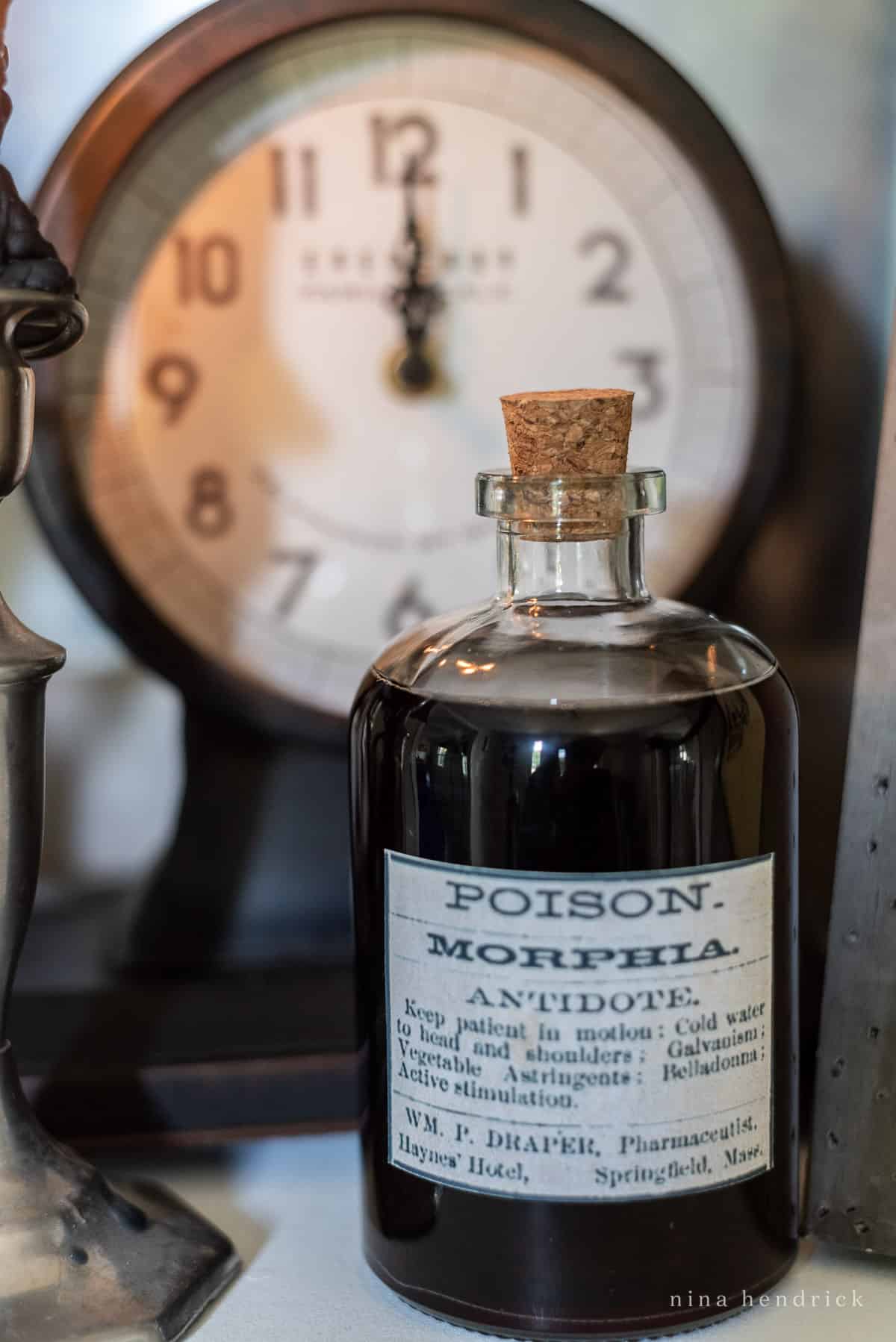 A bottle of faux poison is sitting on a table next to a clock.