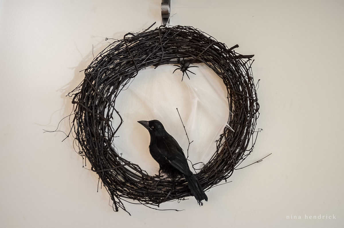 A black crow sits on a wreath of twigs.