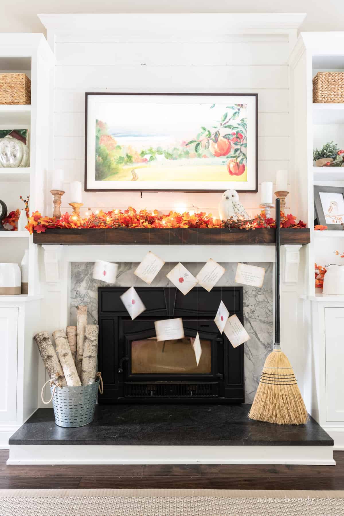 A fireplace mantle decorated with fall leaves and a broom, featuring a Hogwarts acceptance letter.
