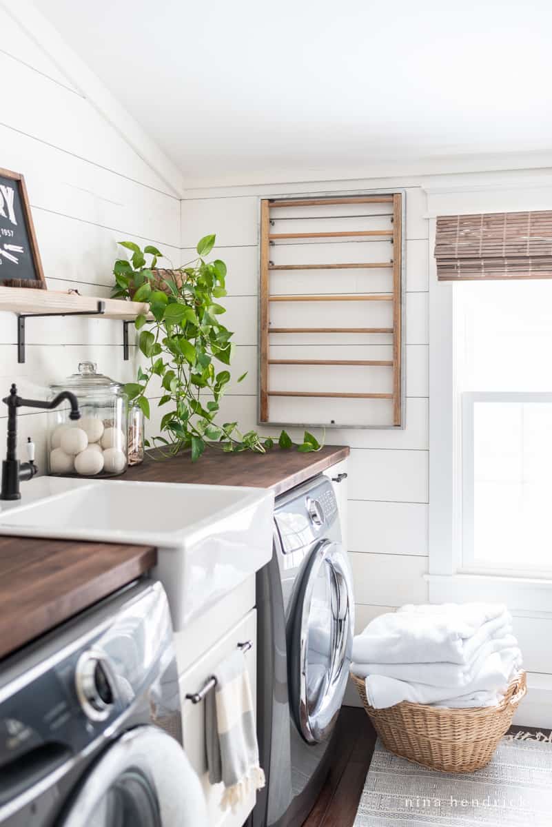 White shiplap laundry room with wicker basket and wall-mounted drying rack 