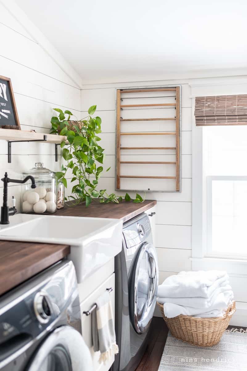 White shiplap laundry room with wicker basket and wall-mounted drying rack