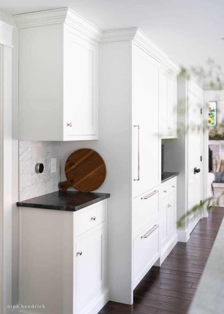 Hidden refrigerator with white cabinetry fronts and a dark countertop beside it