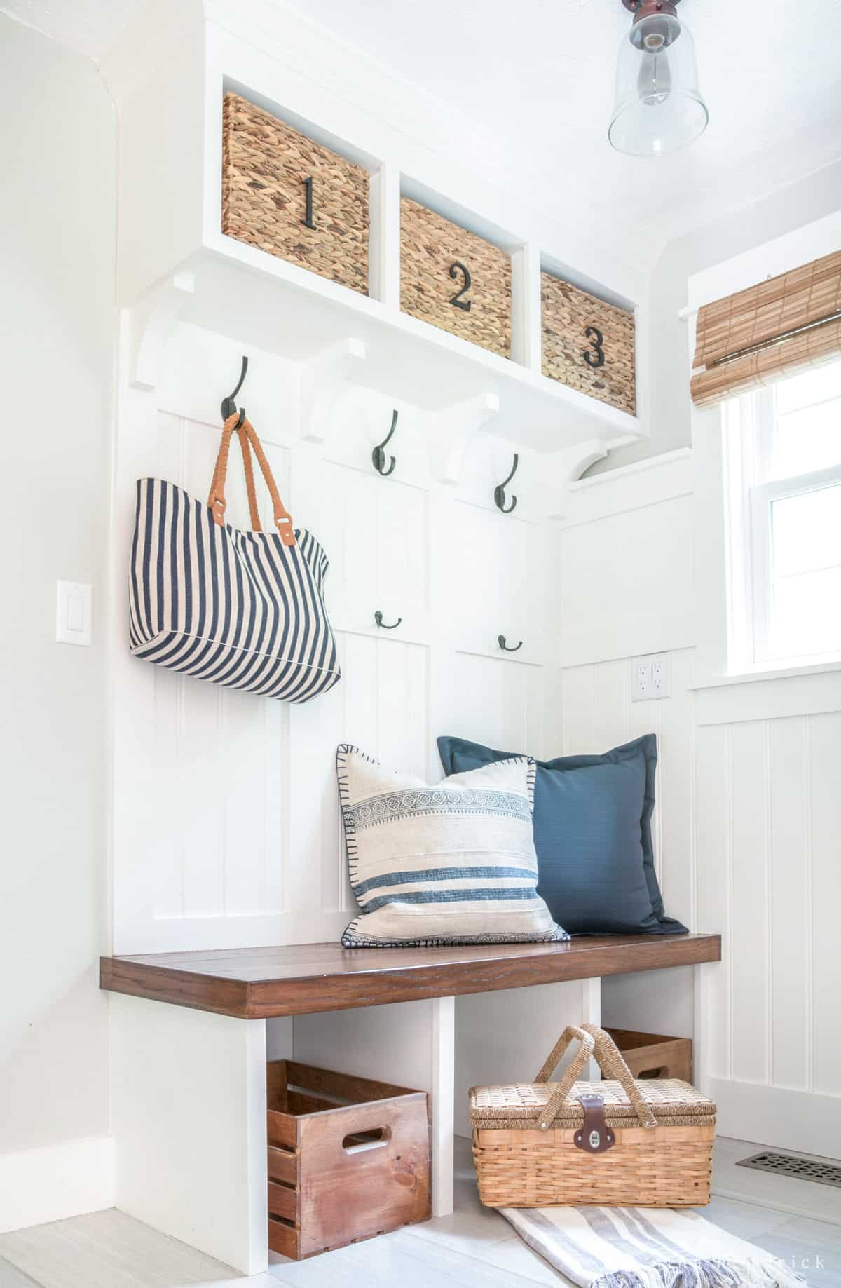 Mudroom home organization with built-in bench, numbered baskets, hooks, and crates.