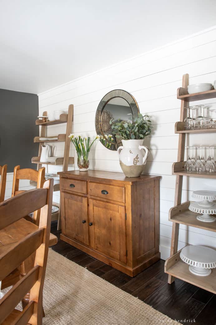 Dining room organization ideas with a buffet and two ladder shelves with serving dishes and glasses.