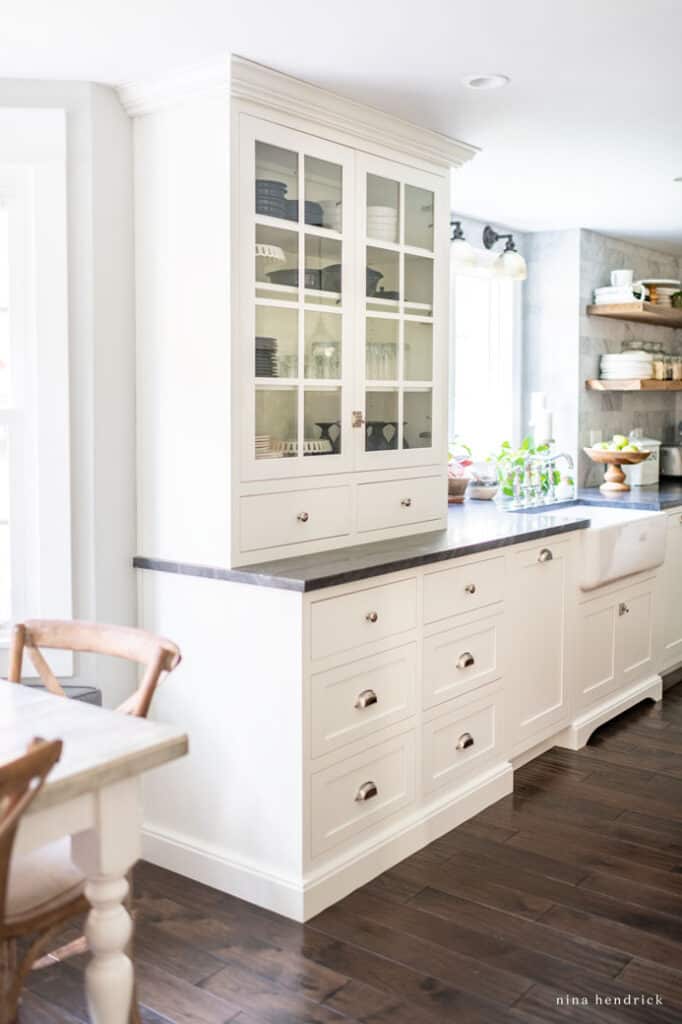 Tall kitchen cabinet with glass doors and dishes and glassware organized inside