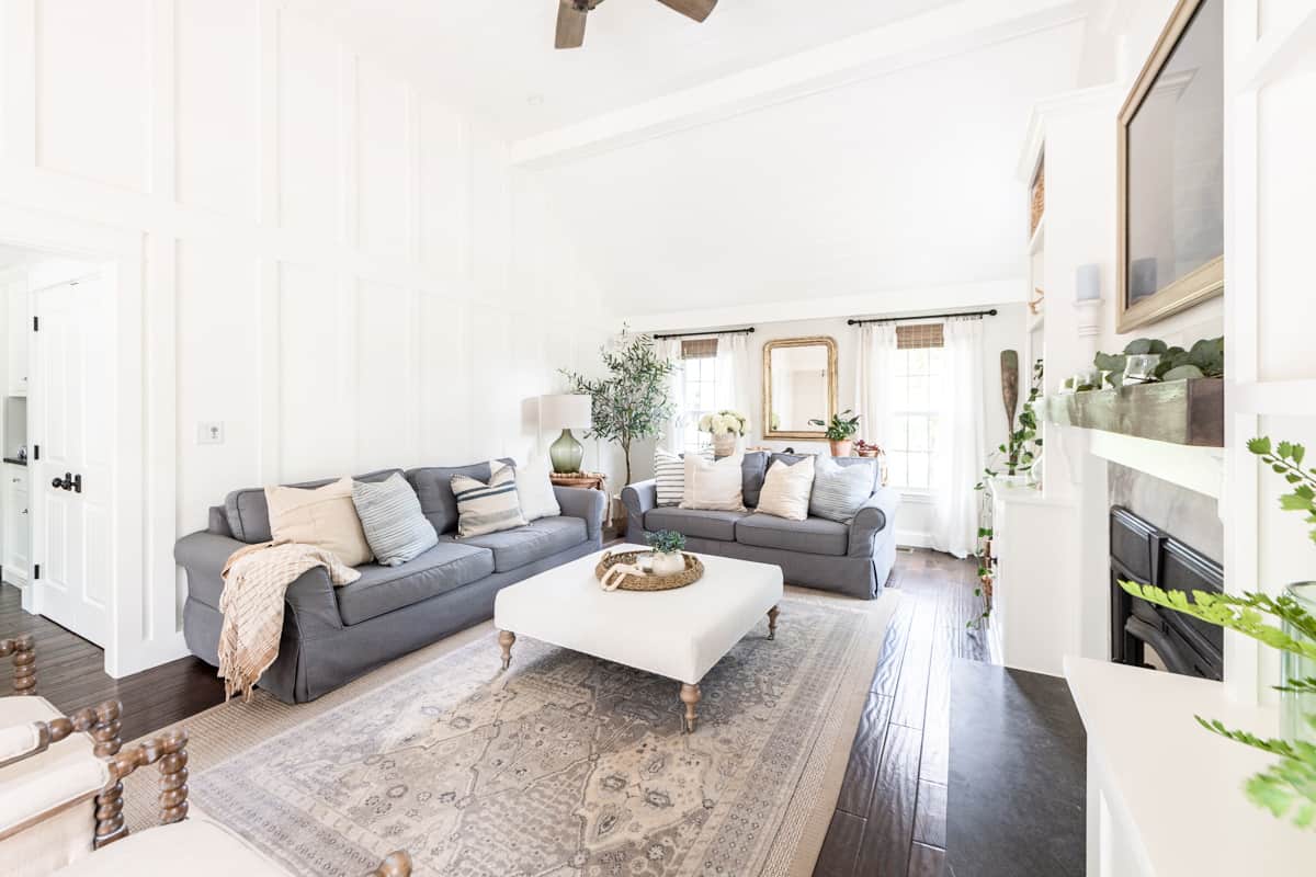 Living room with blue-gray furniture arranged around a white ottoman with a decorative area rug