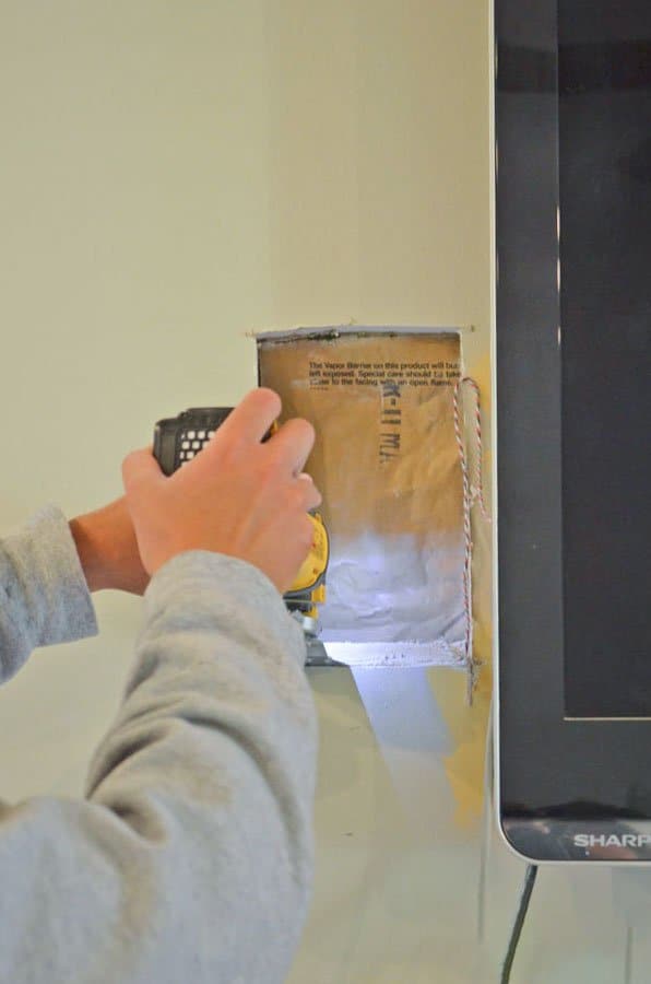 Man cutting hole in the wall to hide wires from a TV above the fireplace.