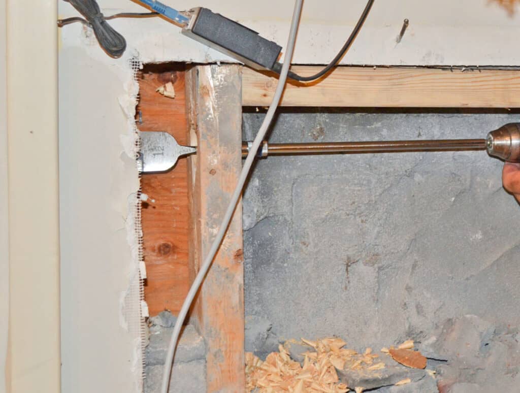 Drilling through studs above a brick fireplace to hide wires behind the tv