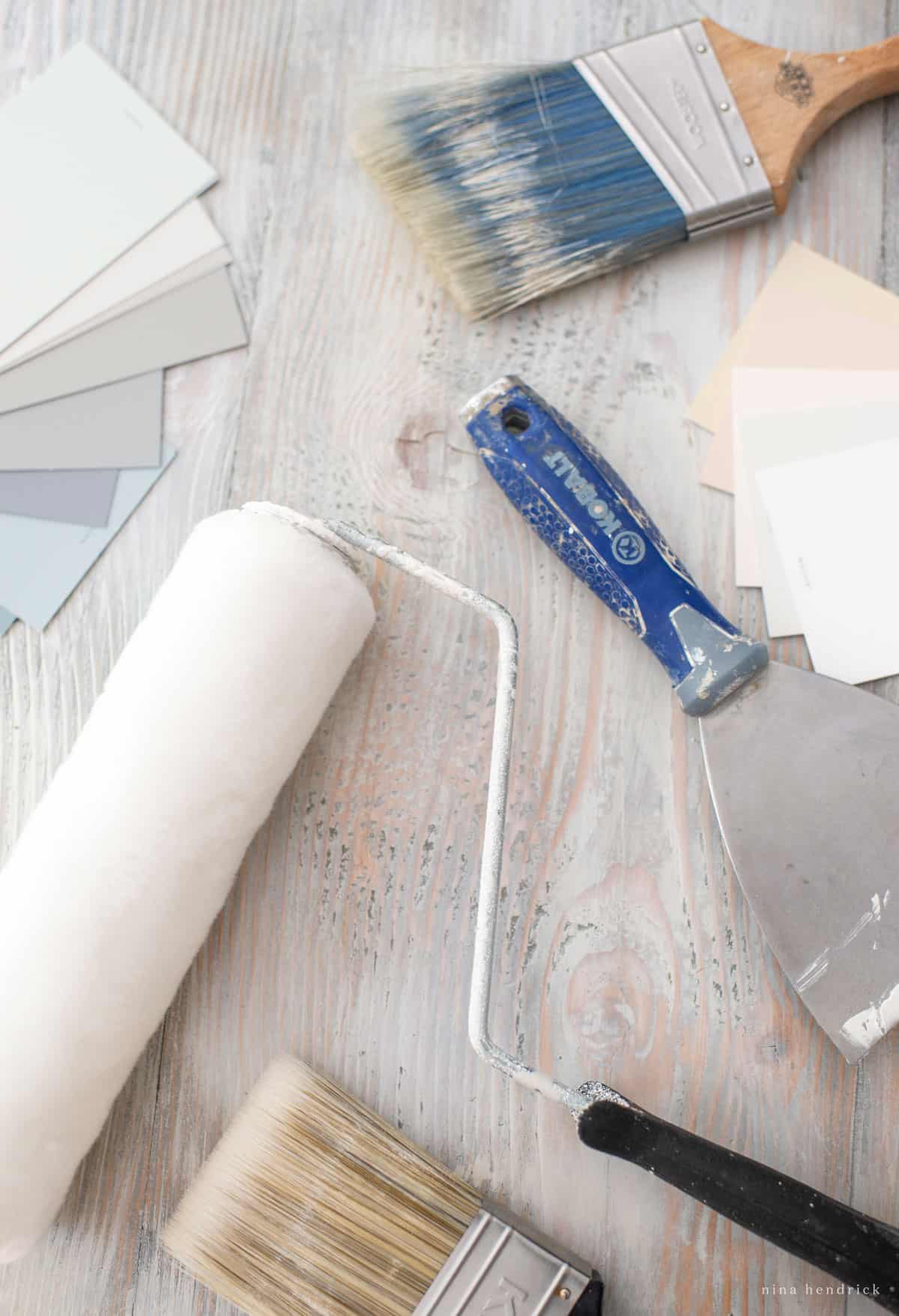 Paint brushes, paint rollers, and paint swatches on a wooden table