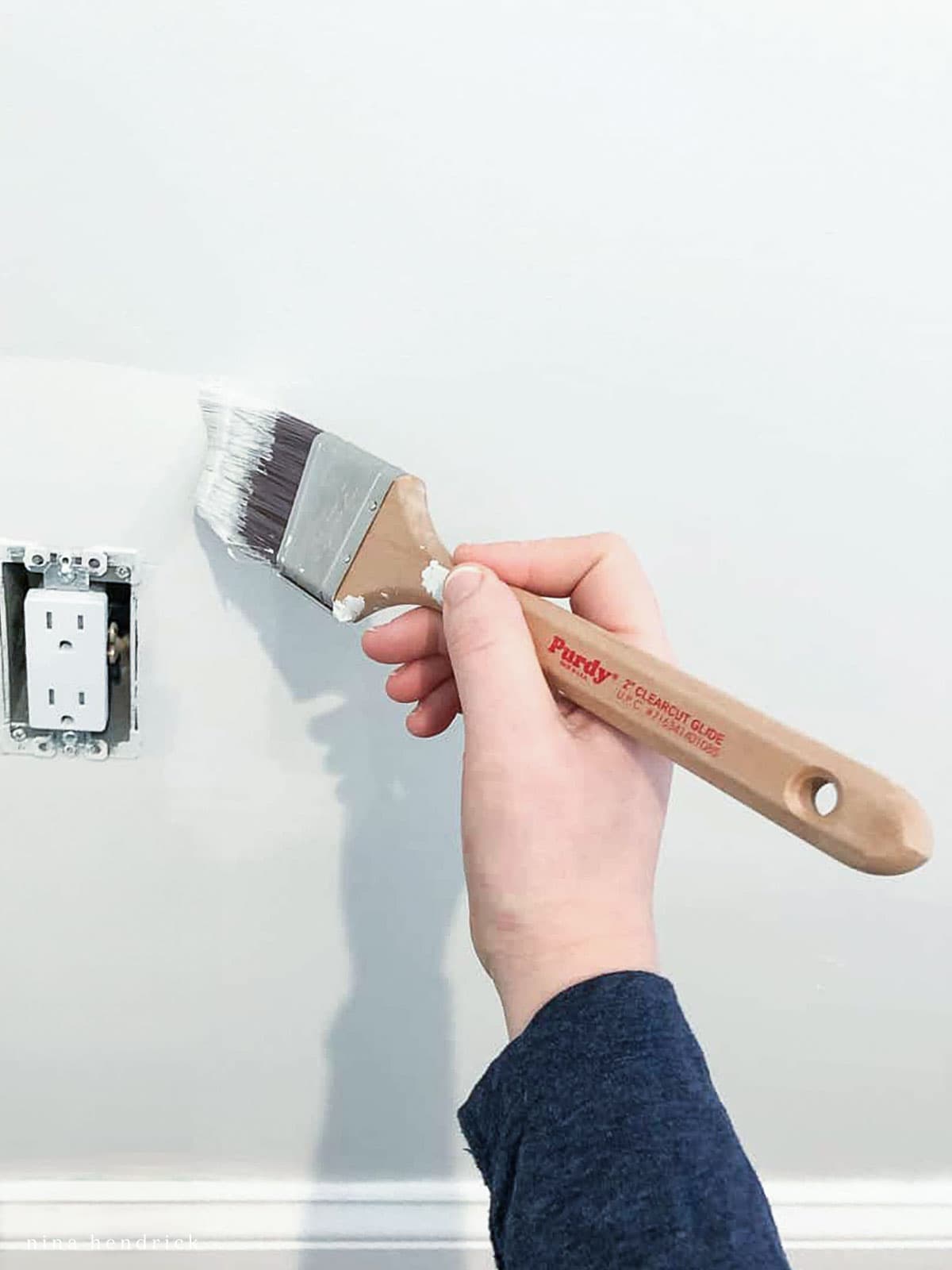 Hand with paintbrush cutting in around a power outlet