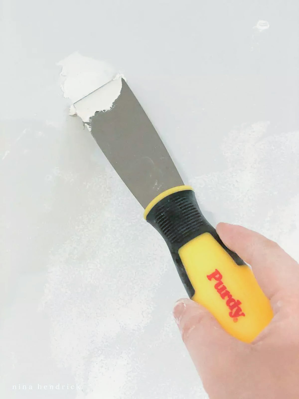 A person using a yellow and black painter's knife to repair a wall
