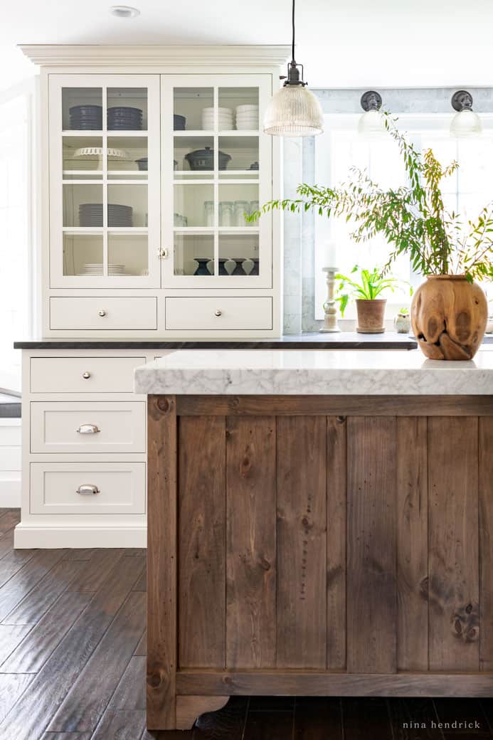 White kitchen cabinets with warm wood brown island and a wooden vase