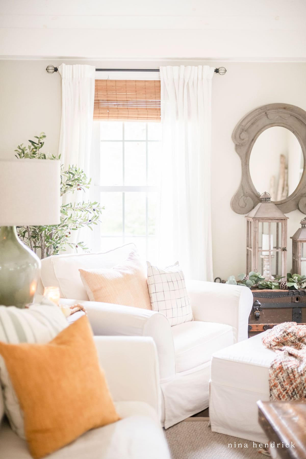 A white living room with orange fall pillows and a mirror.