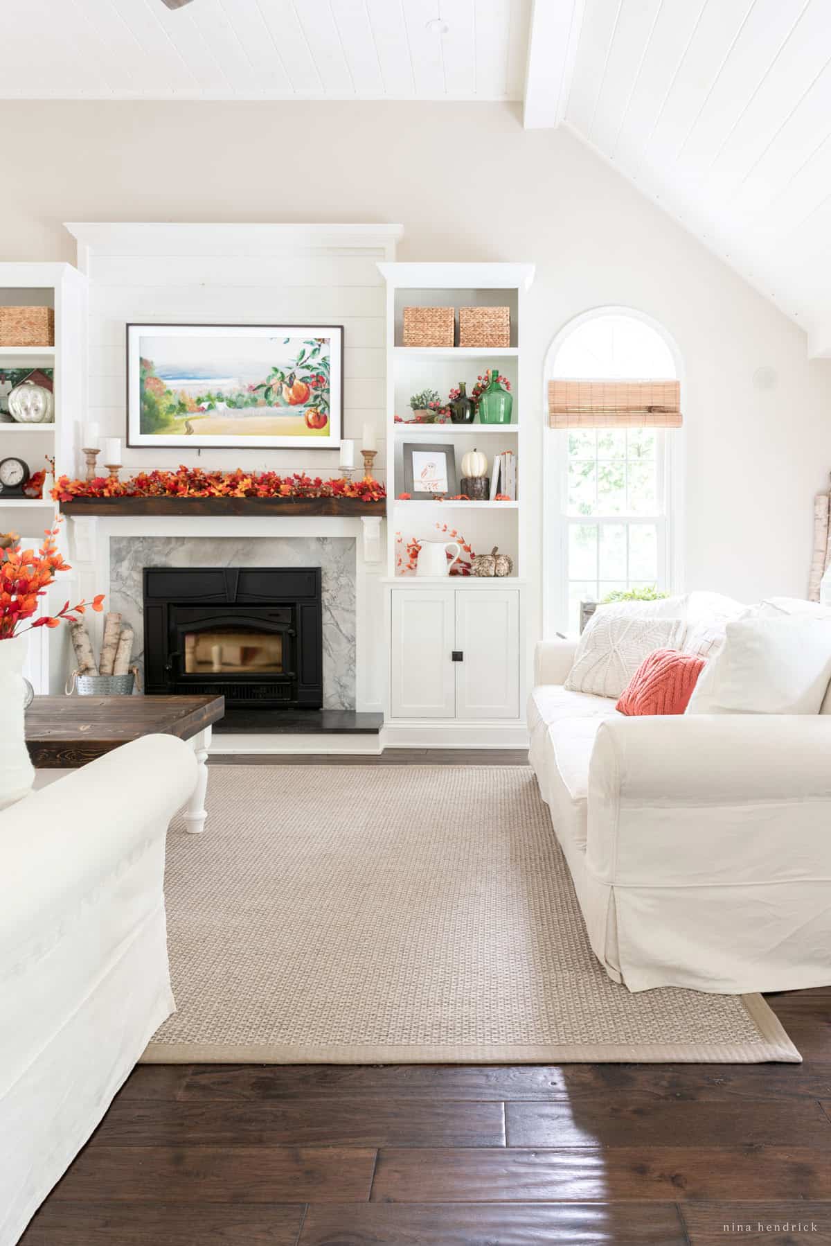 Fall Living Room Decor with pops of orange against white furniture and a fireplace.