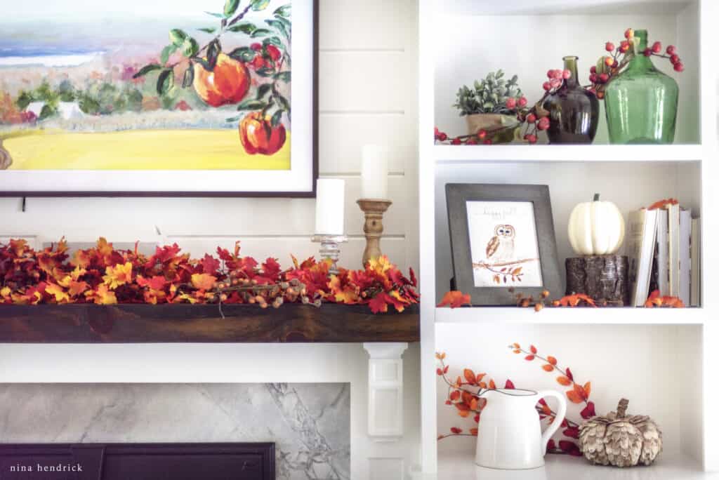 A fireplace mantel decorated with autumn leaves and a painting.