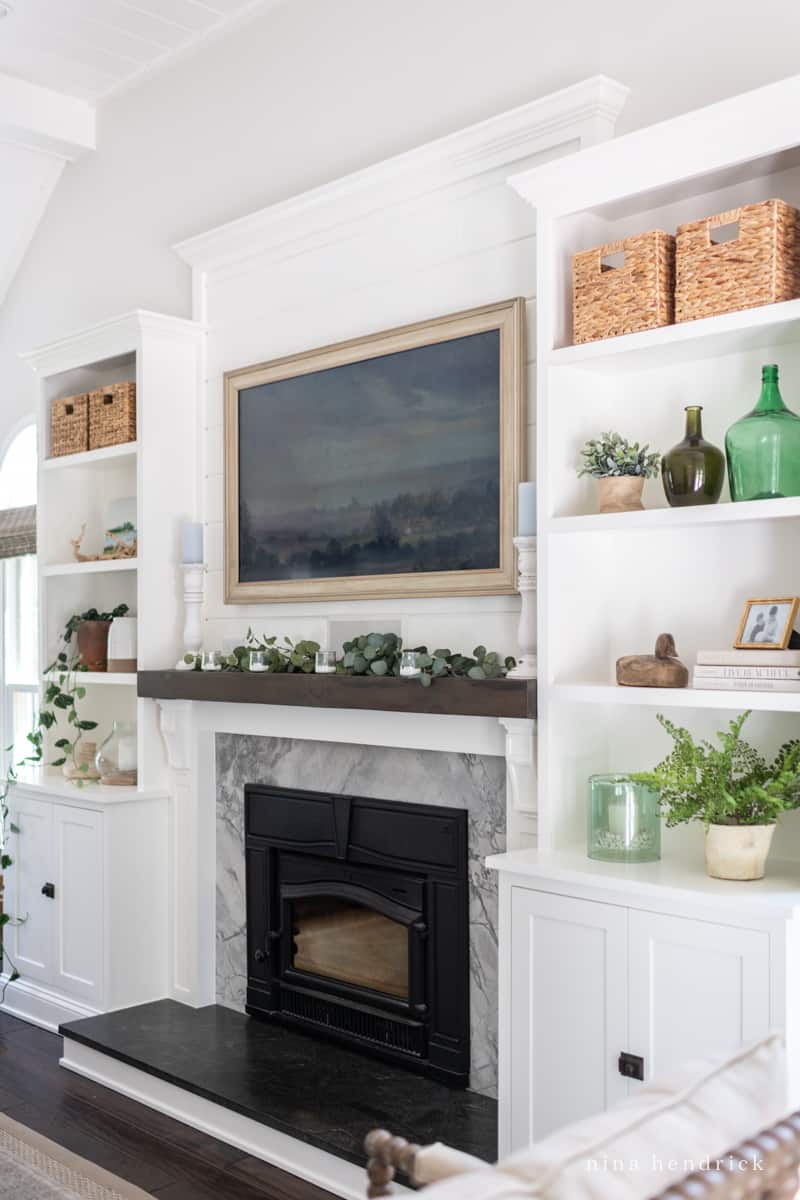 Fireplace built-ins with a dark mantel and neutral decor with a Frame TV featuring landscape artwork