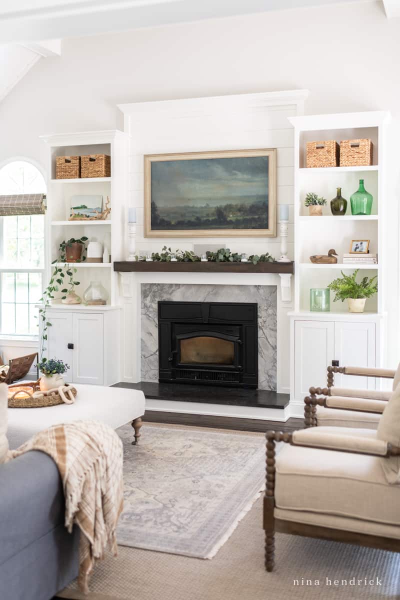 Bright and sunny living room with fireplace built-ins filled with green, blue and wood decor and a Frame TV above the mantel 