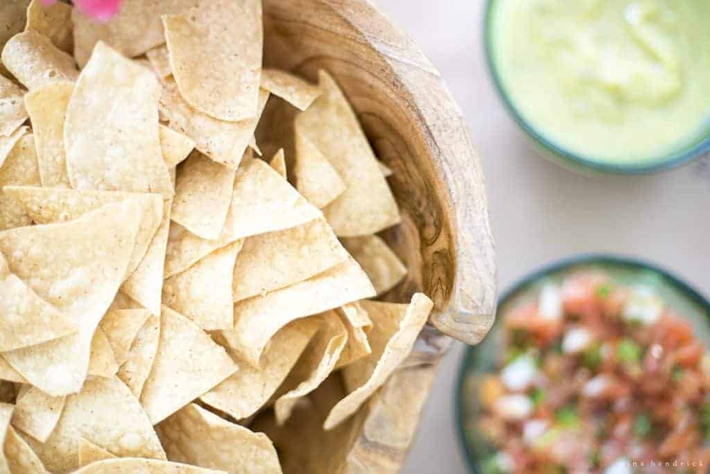 Tortilla chips in a wooden bowl with salsa and guacamole