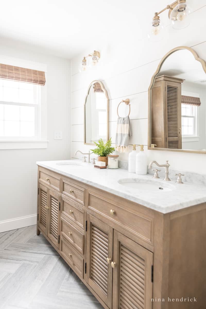 Bathroom vanity with mixed metals: champagne gold pulls, mirror, and light fixtures and brushed nickel faucets. 