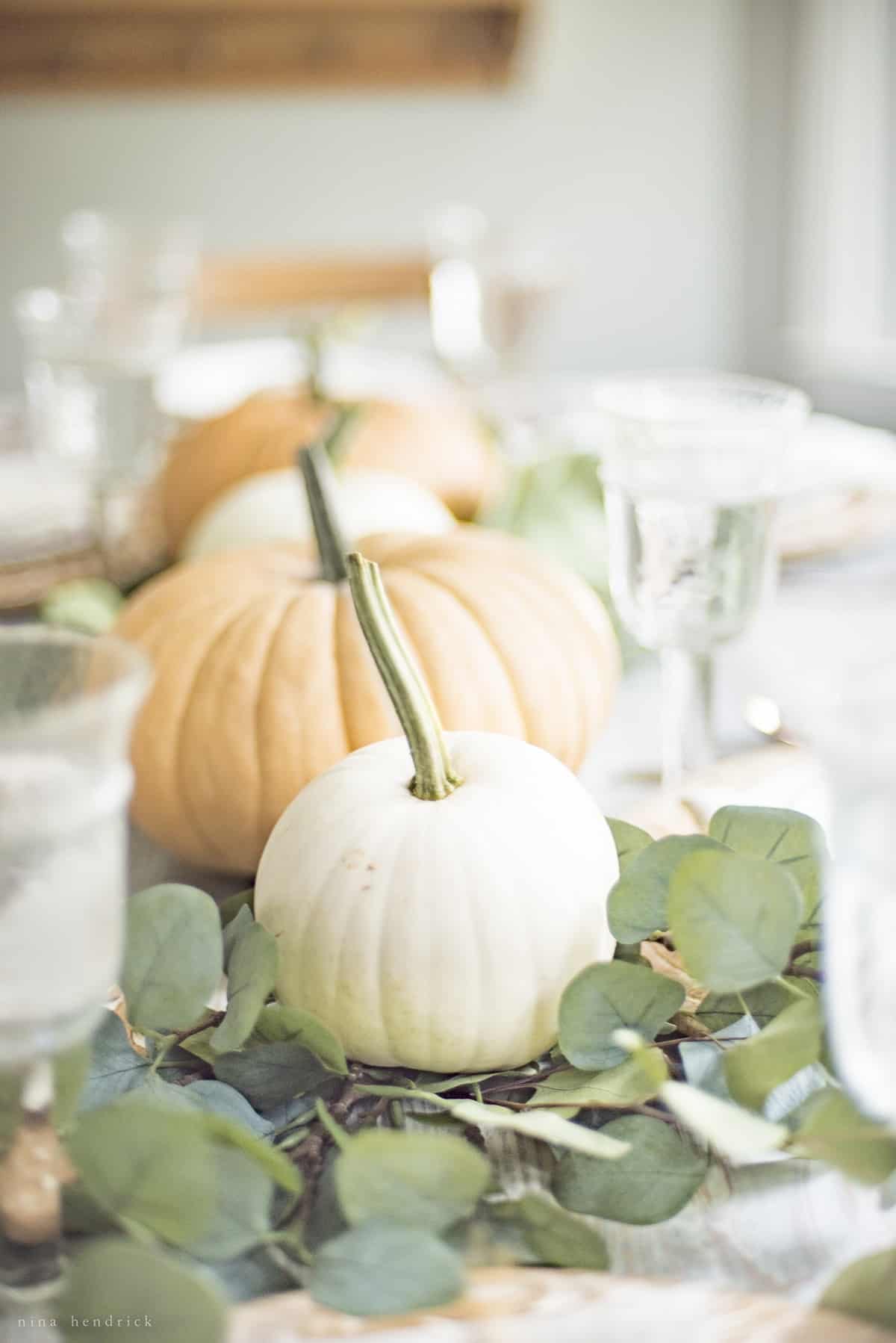 Simple fall tablescape featuring white pumpkins and eucalyptus leaves.